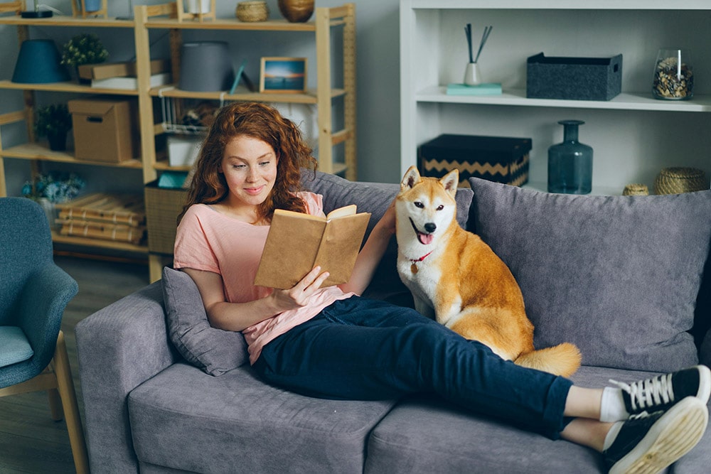 Femme qui lit un livre assise sur un canapé avec son chien
